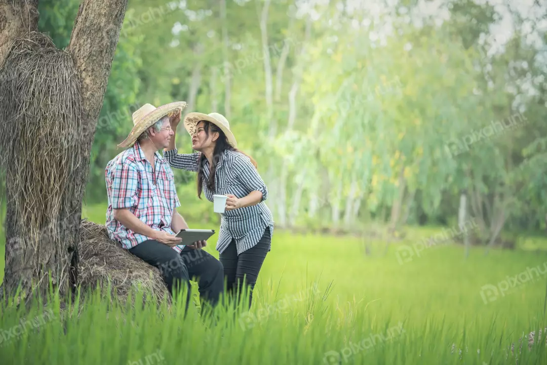 Free Premium Stock Photos A beautiful landscape of a couple sitting on a rock in a lush green field and man is wearing a straw hat and the woman is wearing a sun hat