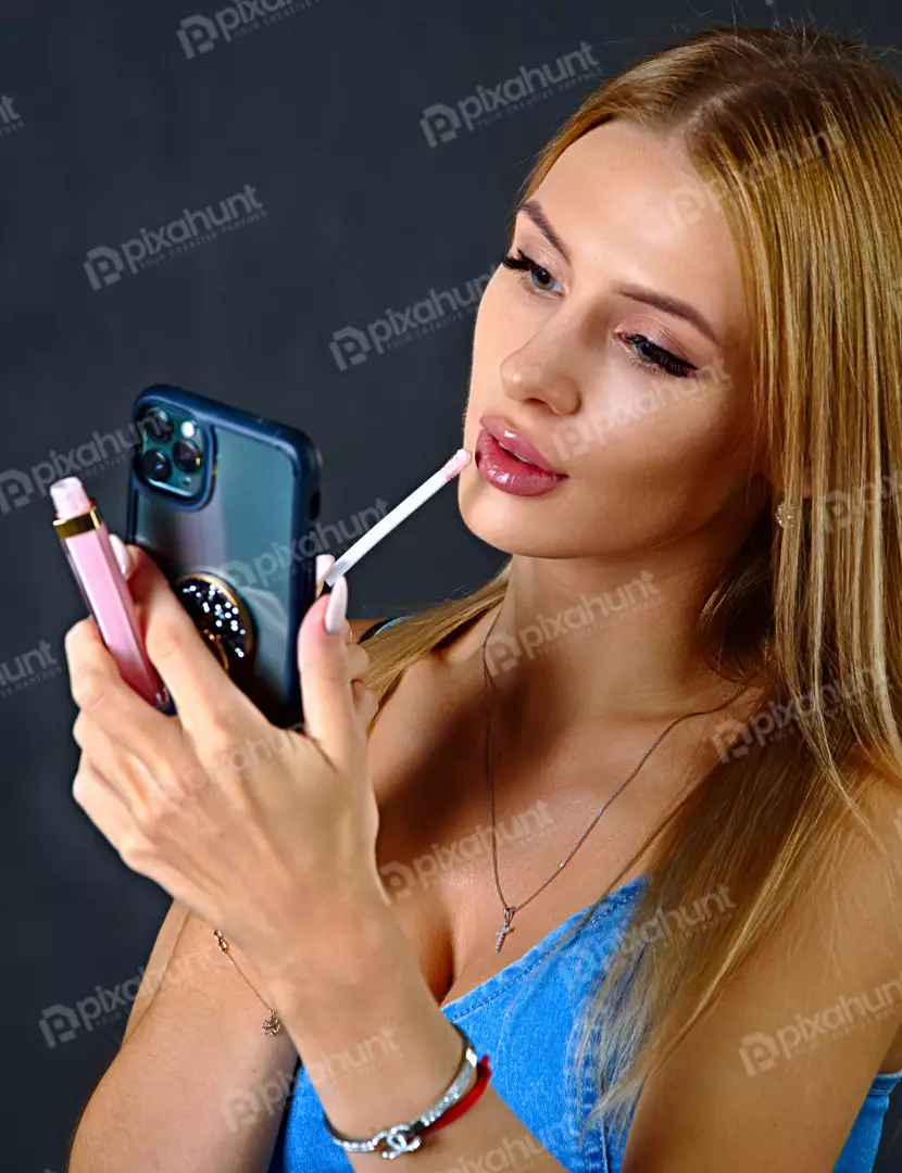 Young Woman Applying Lip Gloss Using Smartphone as Mirror for Beauty Routine