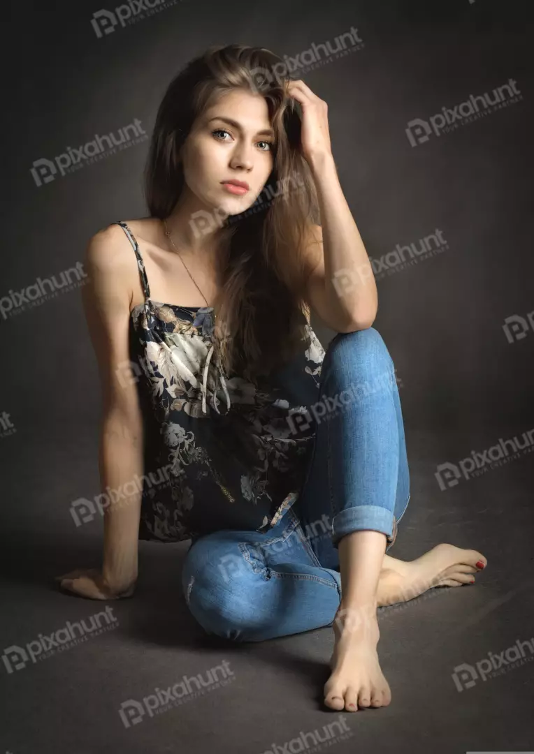 Pensive Young Woman in Floral Camisole and Jeans Sitting Barefoot