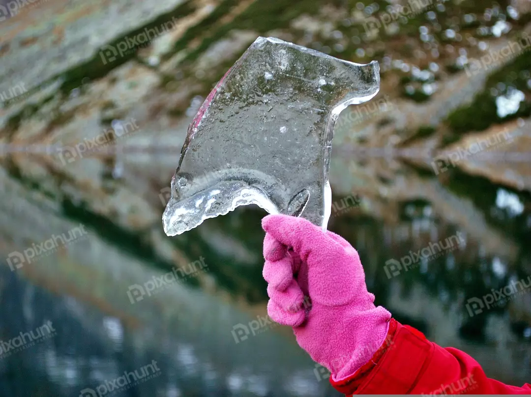 Vibrant Pink Gloved Hand Holding a Translucent Ice Shard in a Cold Winter Landscape