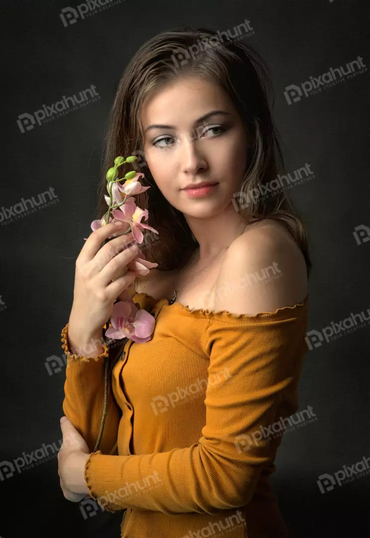 Young Woman in Orange Top Holding Pink Orchid with Thoughtful Gaze
