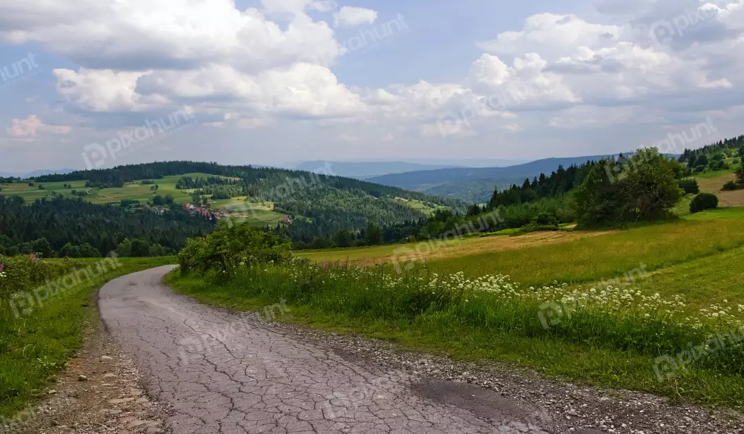 Winding Road Through Lush Green Mountain Landscape with Village and Cloudy Sky