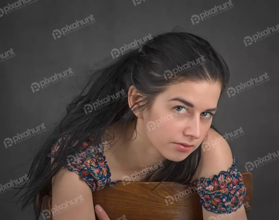 Young Woman Leaning on Chair with Pensive Gaze and Long Dark Hair