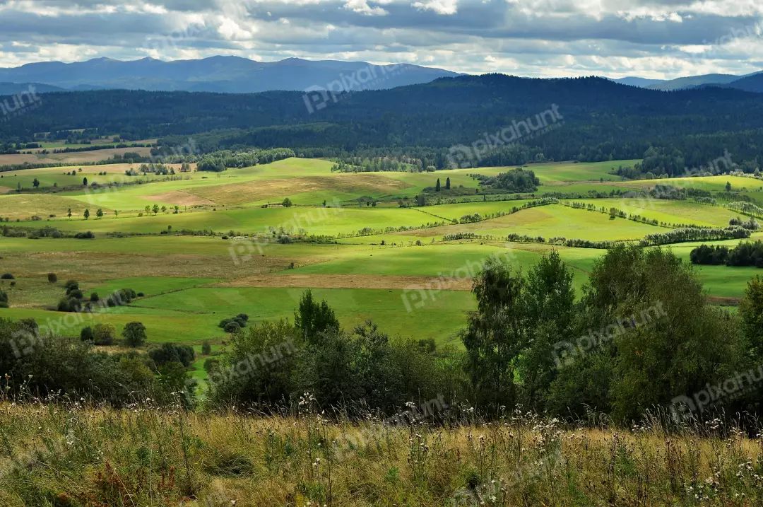 Expansive Green Countryside Landscape with Rolling Hills and Distant Blue Mountains Under a Cloudy Sky