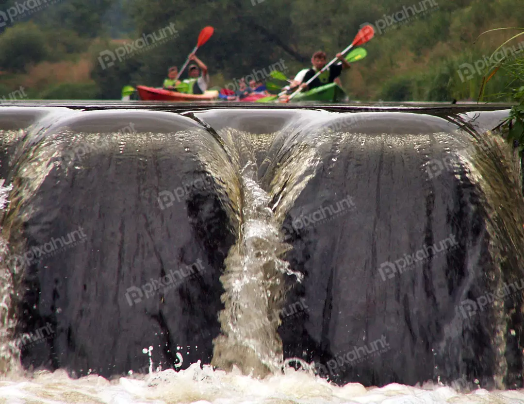 Group of Kayakers Navigating a River Weir with Splashing Water and Lush Green Background