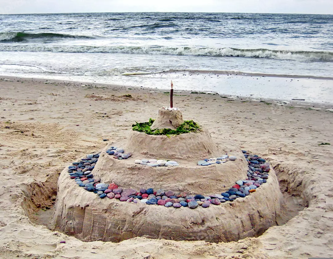 Intricate Sandcastle Creation Decorated with Pebbles and Seaweed on a Coastal Beach