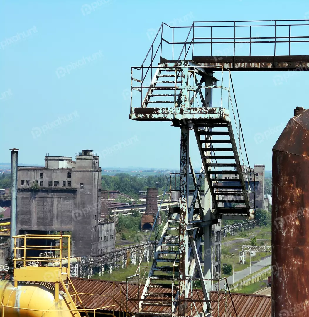 Abandoned Industrial Complex: Rusty Metal Structures, Stairs, and Silos Against a Clear Blue Sky