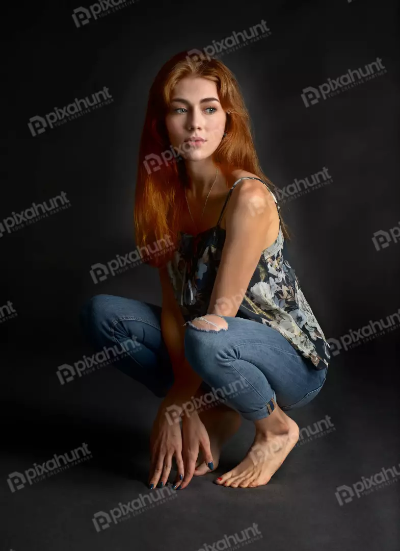 Pensive Young Red-Haired Woman Crouching in Floral Top and Ripped Jeans