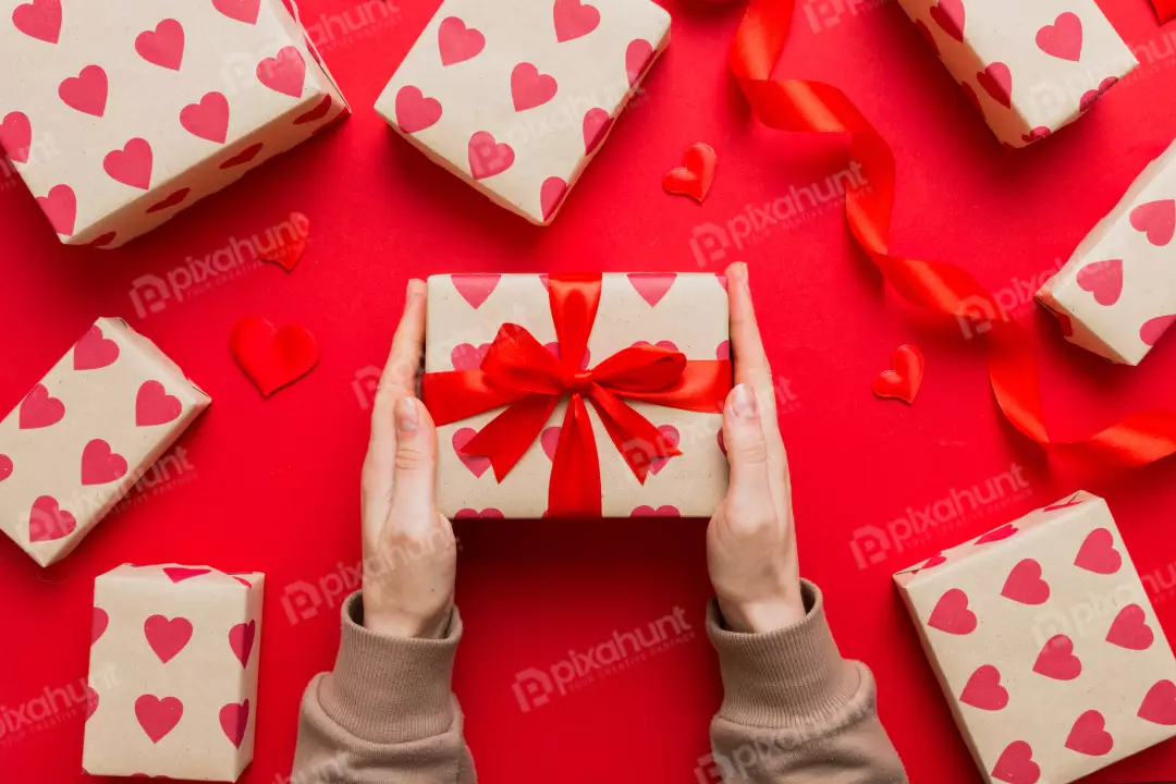 Hands Presenting a Beautiful Heart-Patterned Gift Box on a Romantic Red Background