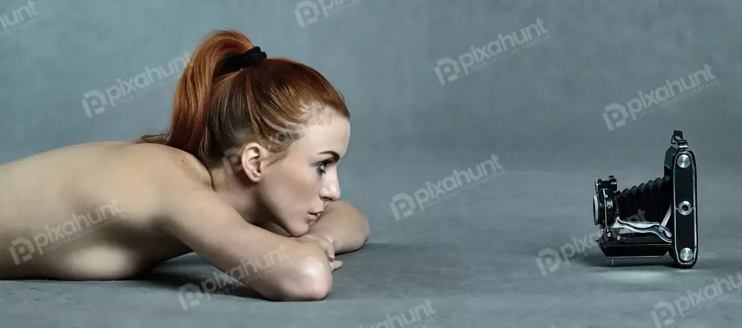 Red-haired Woman Engaged with Vintage Folding Camera on Gray Studio Floor