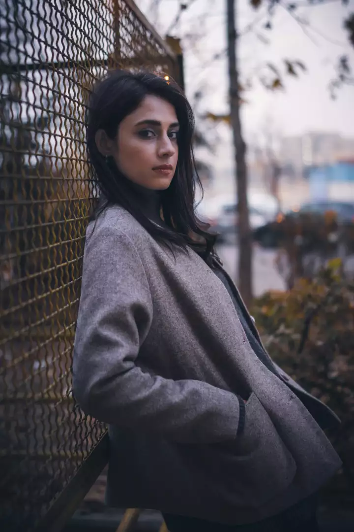 Free Premium Stock Photos Pensive Young Woman in Beige Coat Leaning Against Rustic Metal Fence Outdoors