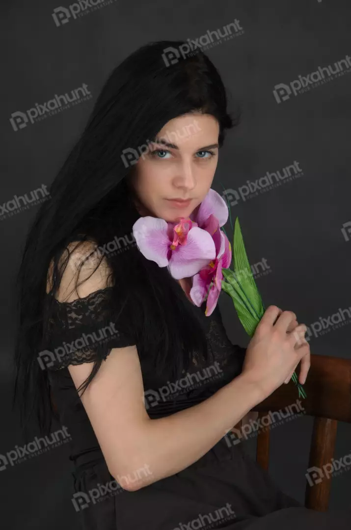 Pensive Young Woman with Long Dark Hair Holding Pink Orchid Flowers