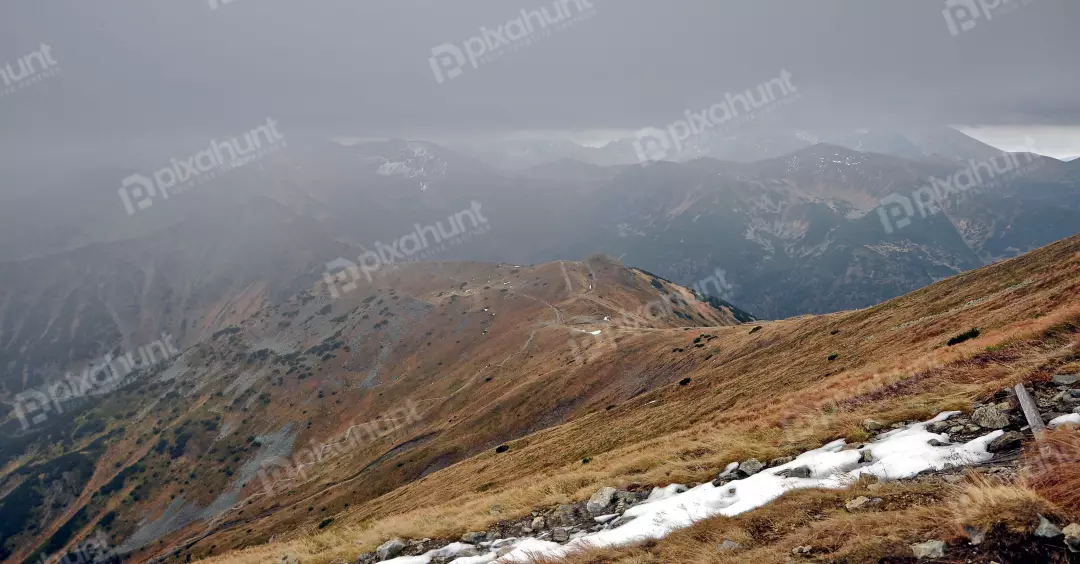 Rugged Mountain Landscape with Winding Trails and Patches of Snow Under Cloudy Skies