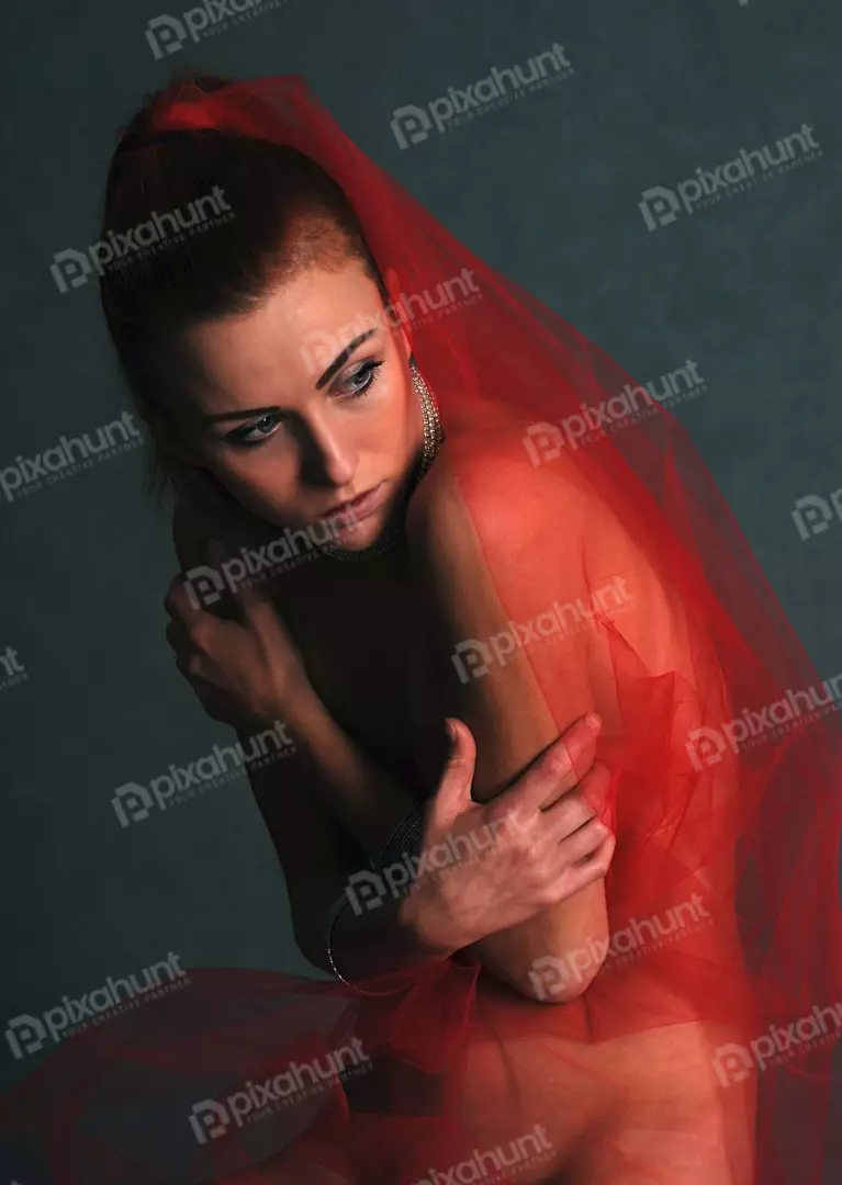 Pensive Young Woman Veiled in Red Sheer Fabric with Elegant Jewelry