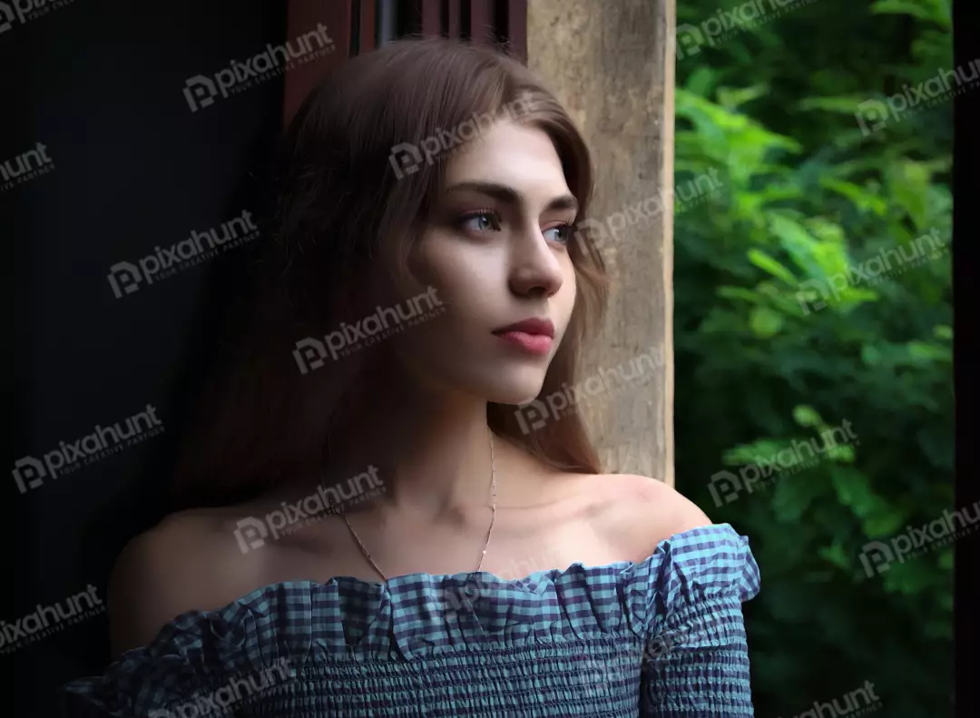 Pensive Young Woman Gazing Outdoors from Window with Lush Green View