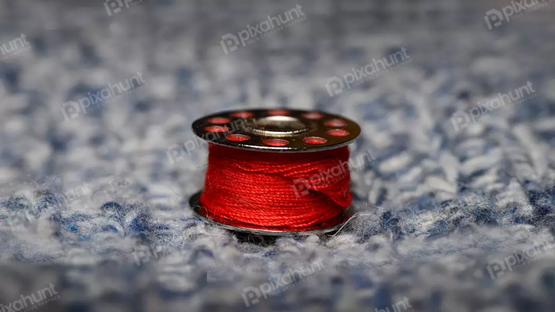 Vibrant Red Sewing Thread Bobbin on Blue Knitted Background