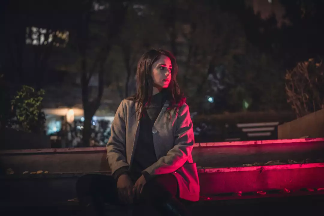 Free Premium Stock Photos Woman in Coat Sitting Outdoors at Night with Red Light Accent