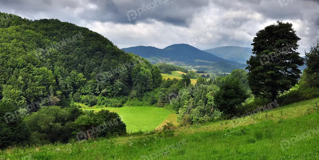Panoramic View of Verdant Mountain Hills and Valley Under Dramatic Cloudy Sky