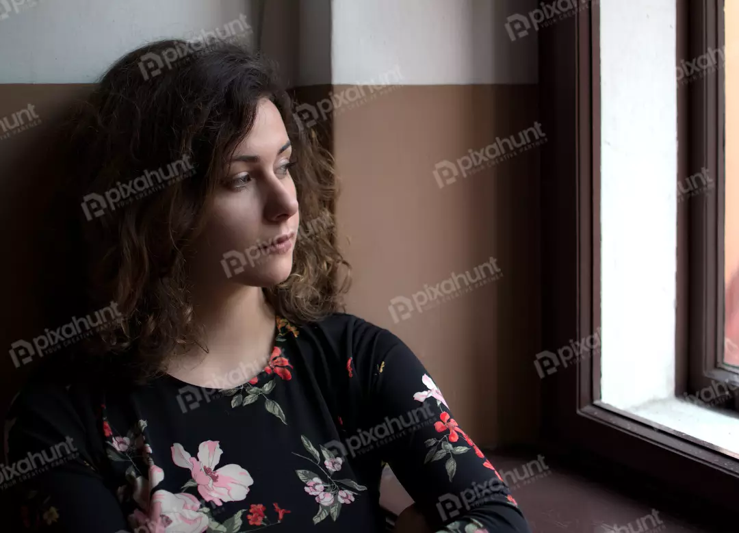 Pensive Young Woman with Curly Hair Gazing Out Window in Floral Top