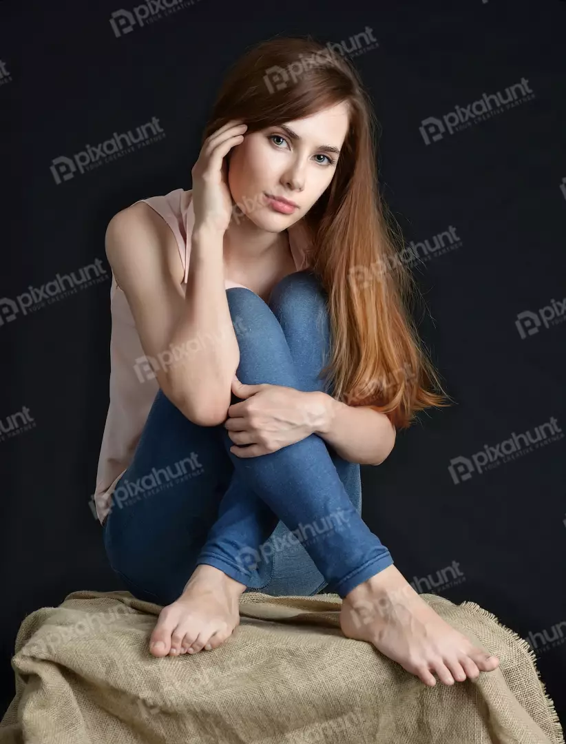 Pensive Young Woman Sitting in Jeans and Pink Top on Burlap