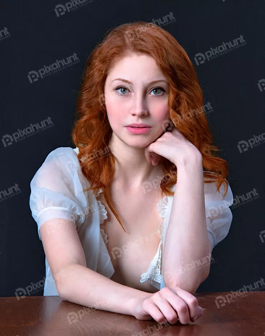 Pensive Redhead Woman with Freckles in Sheer Top at Wooden Table