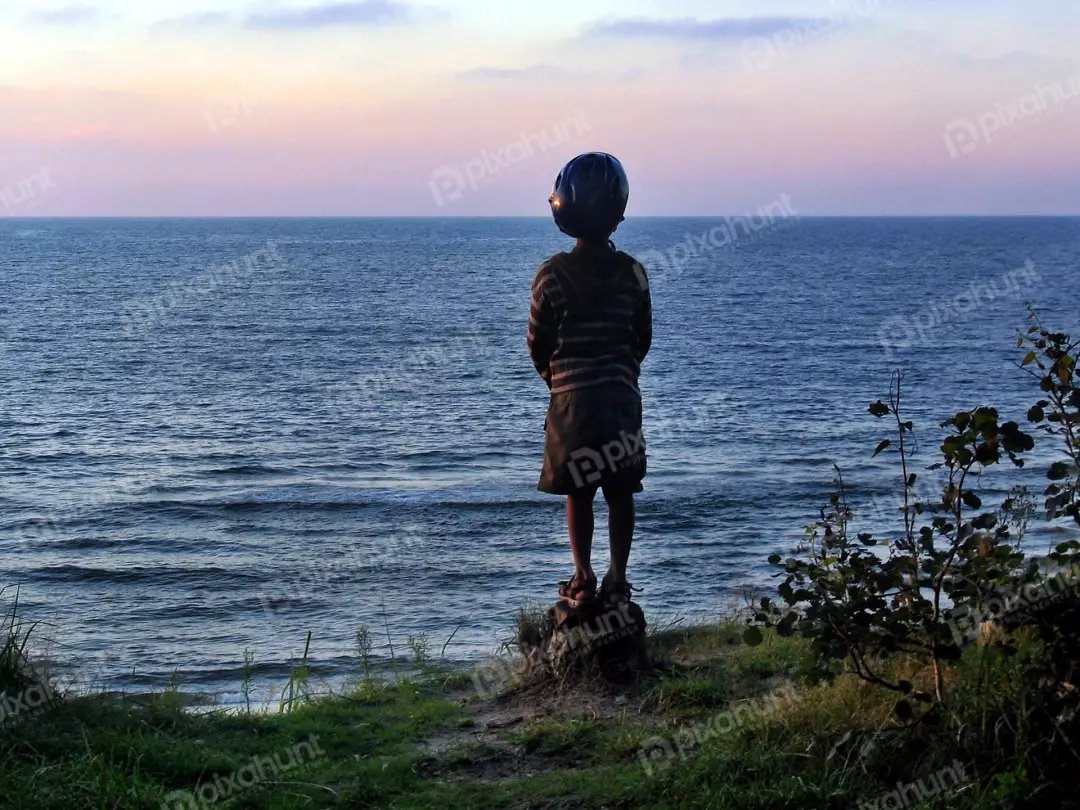 Young Child in Helmet Contemplating Vast Ocean Horizon at Tranquil Sunset