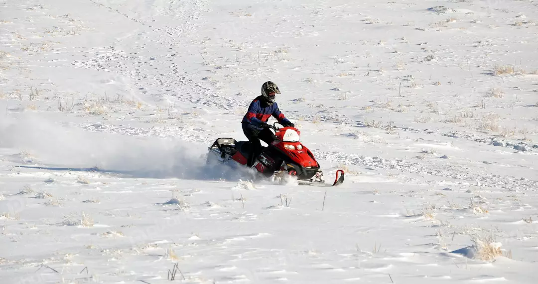 Adventurous Snowmobile Rider Navigating Winter Snow Field with Dry Grass