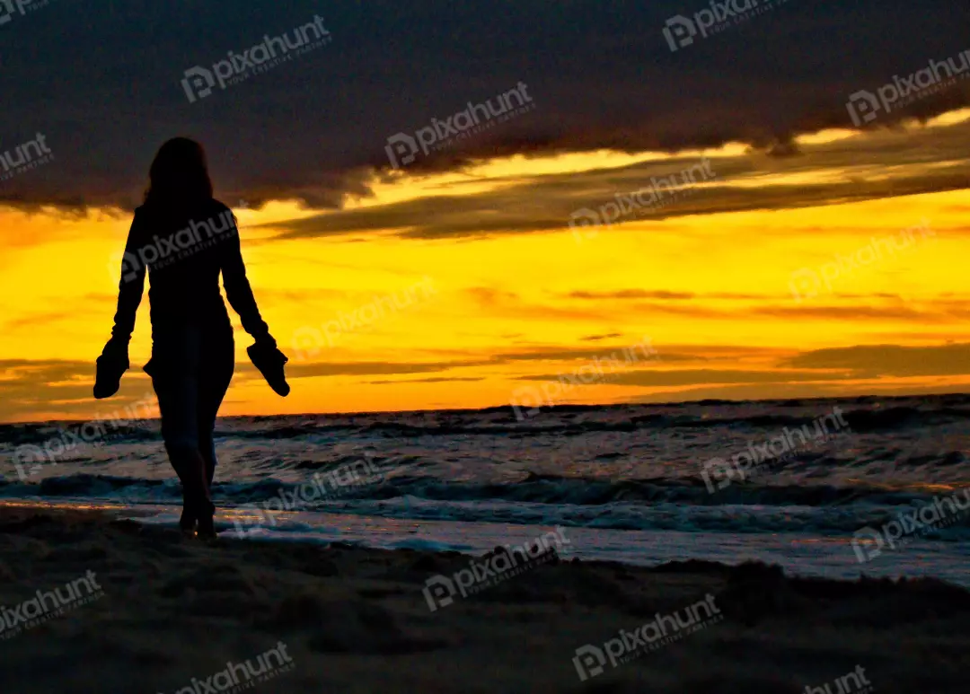 Woman's Silhouette Walking on Tranquil Beach at Golden Sunset Hour