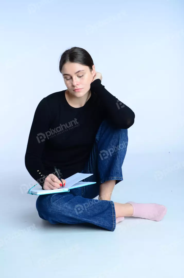 Focused Young Woman Writing in Blue Notebook on White Background