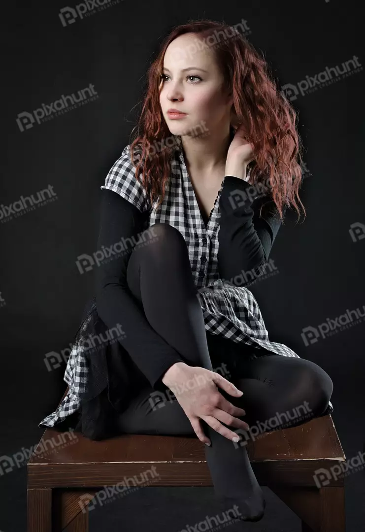 Redhead Woman in Plaid Shirt Sitting Thoughtfully on Dark Background