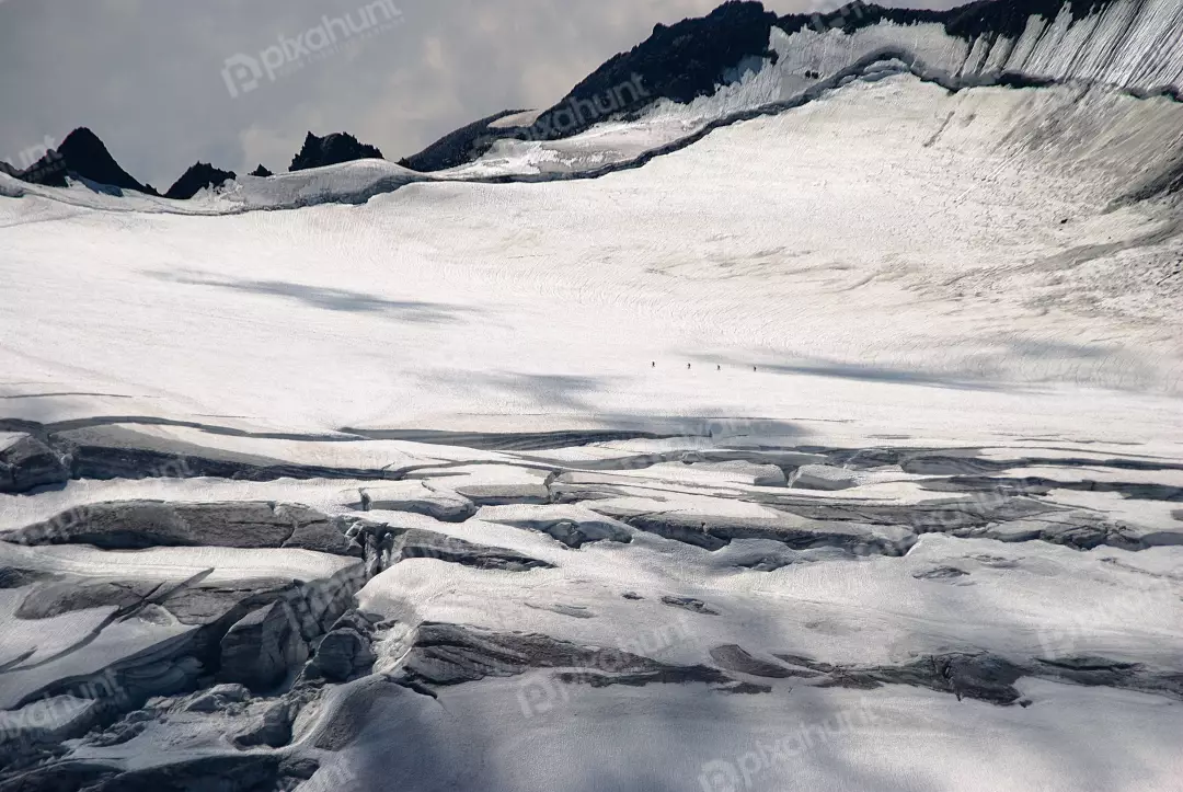 Mountaineers traversing a vast glacier with deep crevasses under dramatic cloudy skies