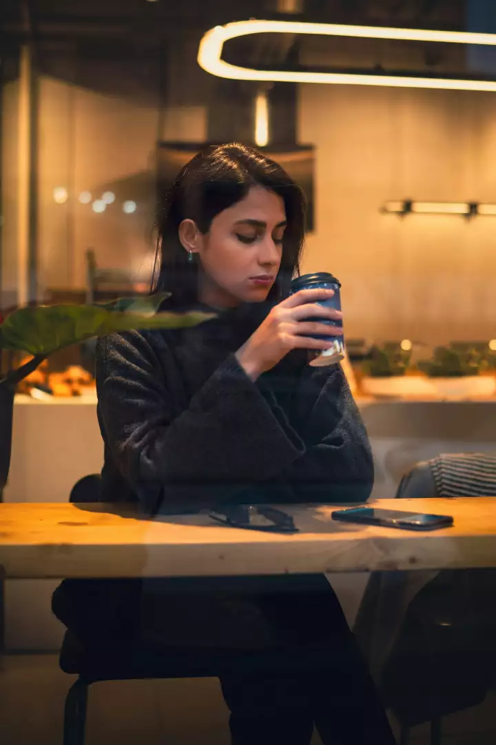 Free Premium Stock Photos Young Woman Sipping Coffee in Contemplative Moment at Atmospheric Evening Cafe