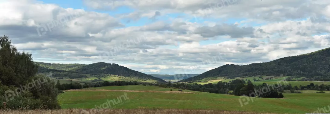 Panoramic Green Valley with Forested Mountains, Lush Fields, and Cloudy Sky