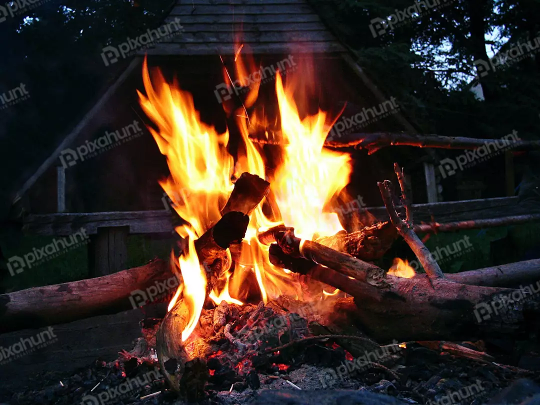 Bright Campfire Burning with Vivid Flames Against Dark Rustic Cabin at Dusk