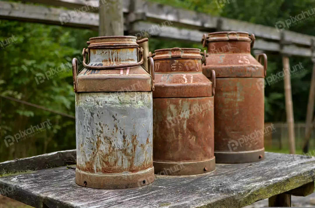 Rustic Weathered Metal Milk Cans Displayed on Old Wooden Table Outdoor