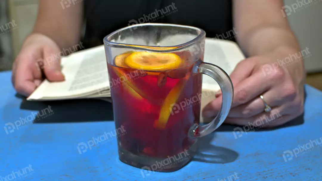 Woman's Hands Holding Open Book While Enjoying Warm Lemon Berry Tea