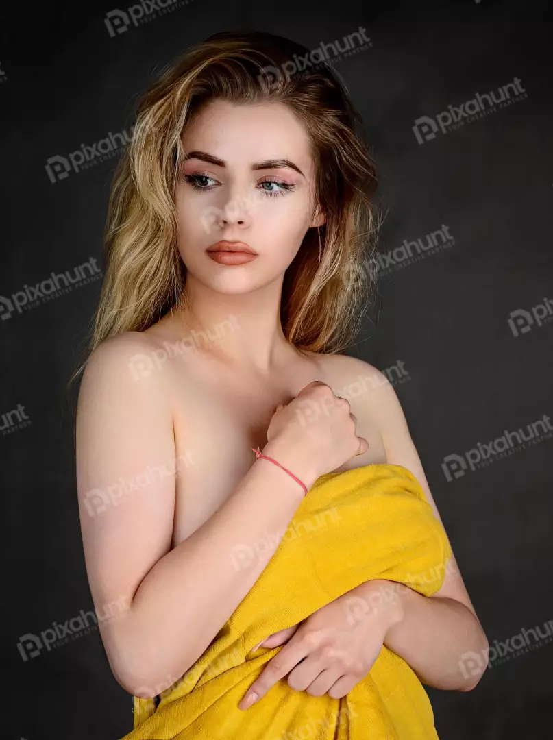Pensive Young Woman Draped in Yellow Towel with Wavy Blonde Hair