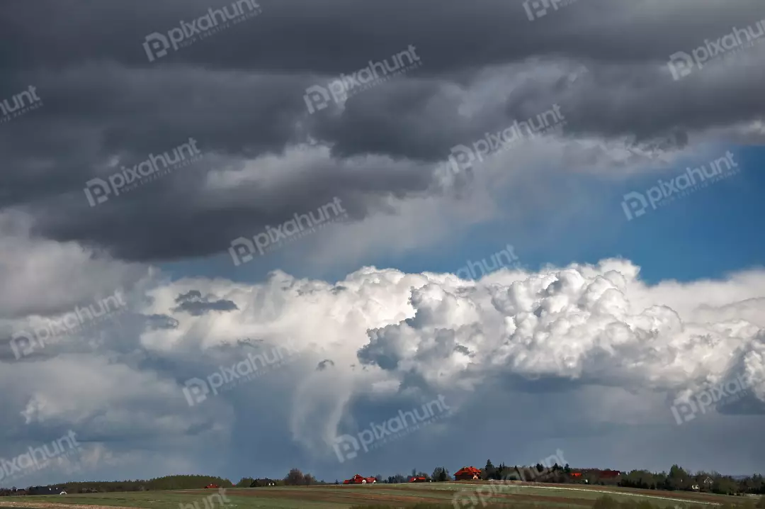 Dramatic Storm Clouds Gathering Over Rural Landscape with Distant Houses and Blue Sky