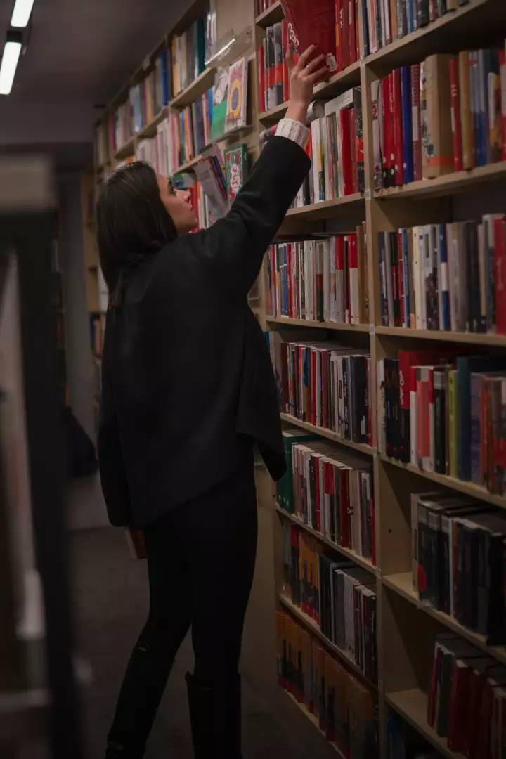 Free Premium Stock Photos Young Woman Reaching for a Red Book on a Bookshelf in a Bookstore