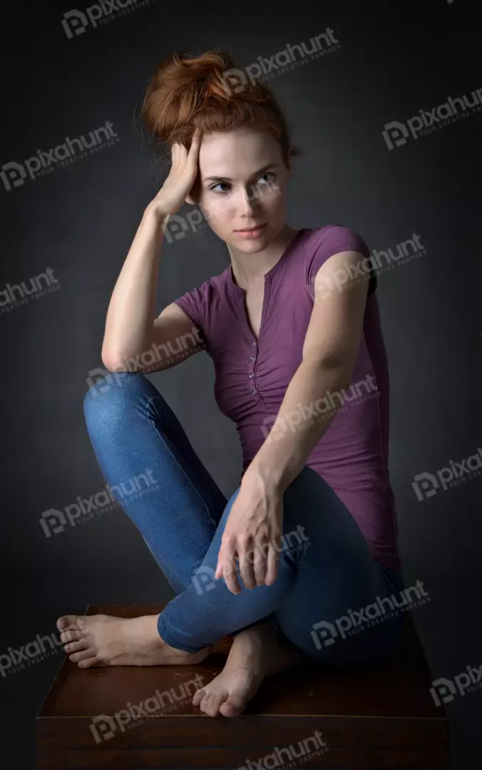 Pensive Young Woman with Red Hair and Blue Jeans Sitting Contemplatively