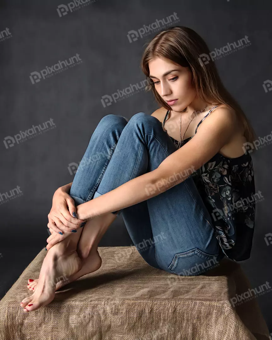 Young Woman Sitting Thoughtfully in Blue Jeans and Floral Camisole