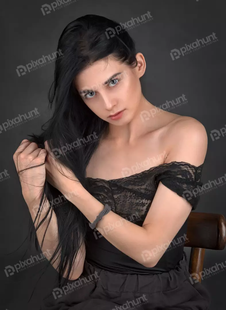 Pensive Young Woman Gently Pulling Long Black Hair in Black Lace Top