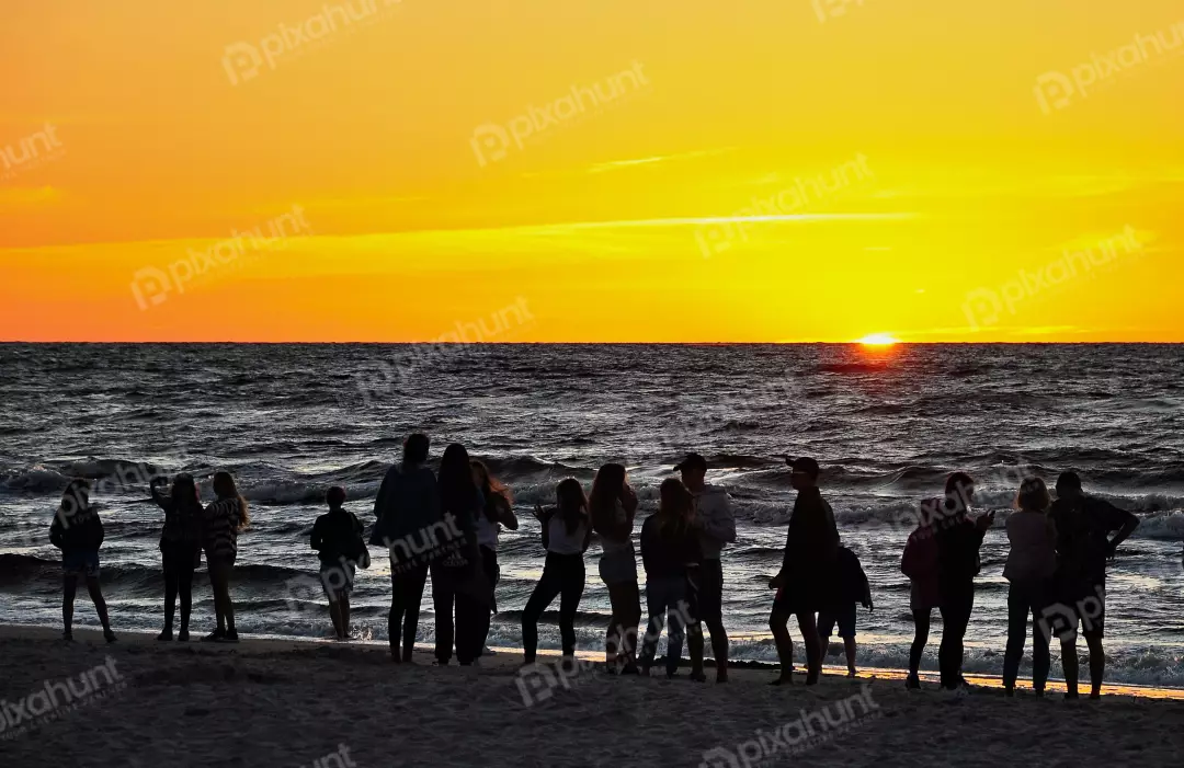 Silhouettes of friends and family watching a breathtaking golden sunset over the tranquil sea
