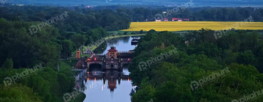 Historic Aqueduct Illuminated at Twilight over Winding River with Vibrant Rapeseed Fields