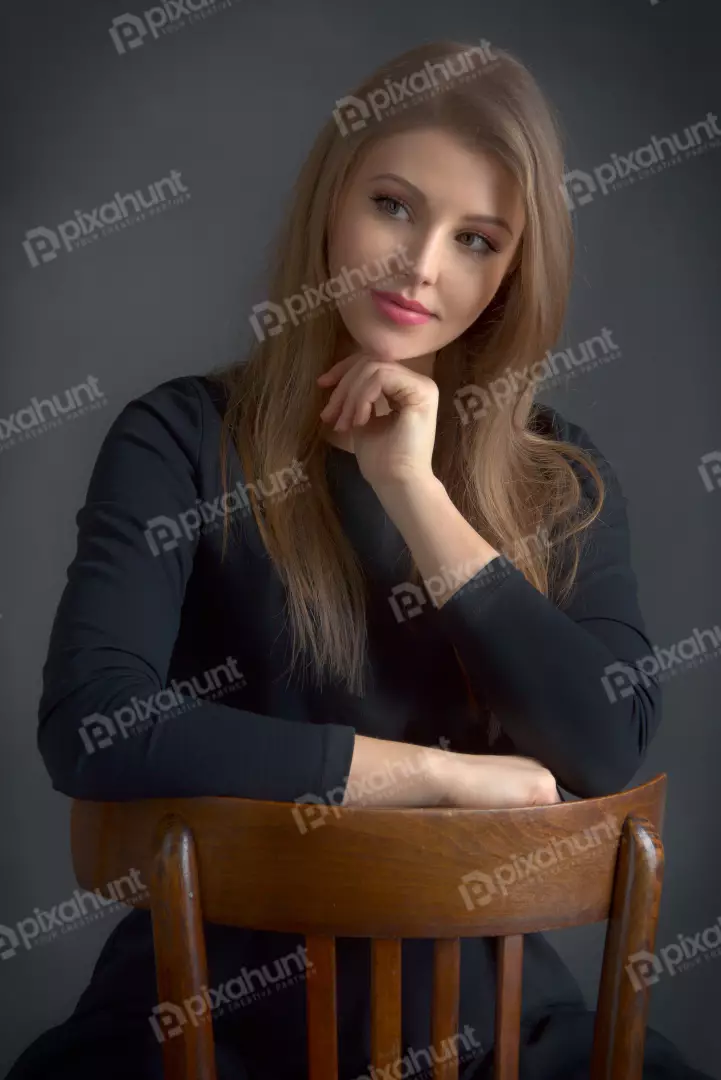 Elegant Young Woman with Long Blonde Hair Posing Thoughtfully on Wooden Chair