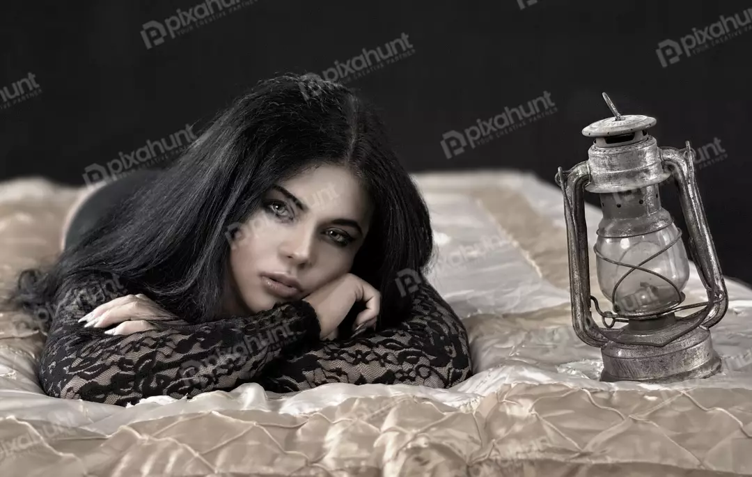 Pensive Woman with Long Dark Hair and Vintage Lantern on Elegant Bed