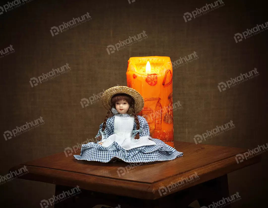 Vintage Doll with Straw Hat Beside Glowing Orange Candle on Wooden Table