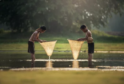 Two little boys fishing in a river and boys are both wearing shorts and no shirts, and they are both standing in the water