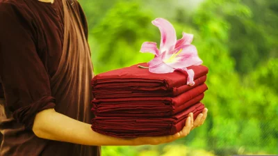 A Monk holding a stack of red cloths With flower