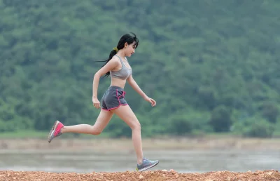 A young woman running in a park and wearing a grey sports bra with black shorts